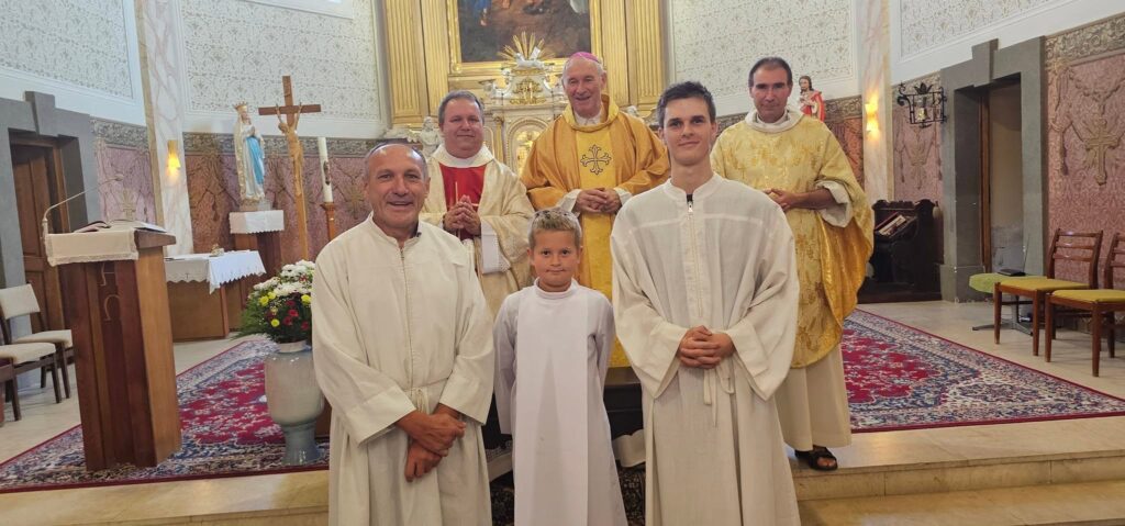 Priester und Ministranten stehen vor einem Altar.